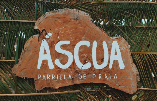 Nome do restaurante Áscua talhado na madeira. O restaurante de parrilla fica na Praia do Marceneiro, na Rota Ecológica dos Milagres, em Alagoas